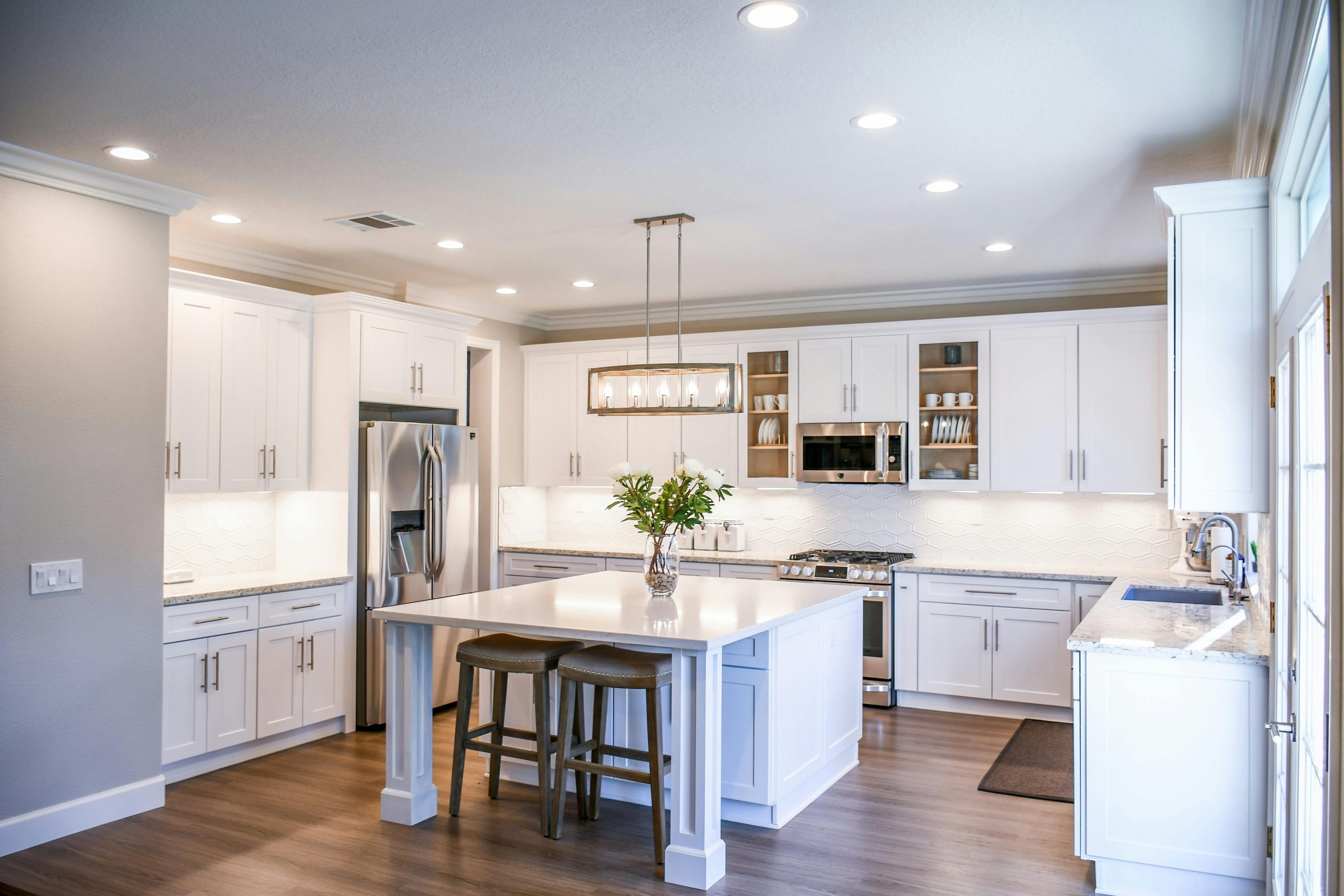 Services Elegant white kitchen featuring an island, modern appliances, and ample natural light.